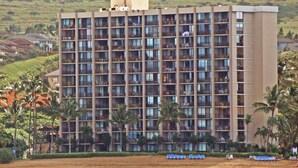 Ein mehrstöckiges Hotel mit Balkonen in Strandnähe, mit Palmen und einem Sandstrand.
