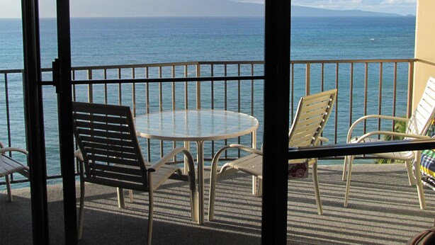 Ein Balkon mit Glastisch und Stühlen, mit Blick auf ein Gewässer und entferntes Land.