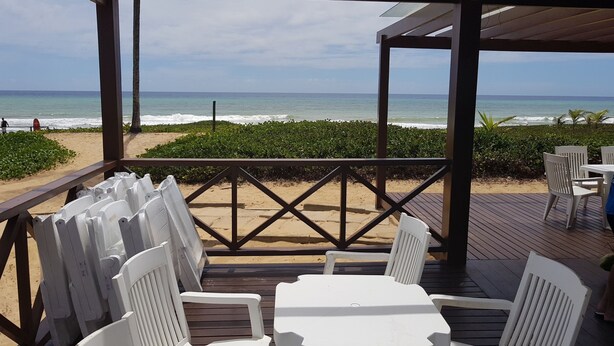 Um terraço à beira-mar com cadeiras e mesas de plástico branco, com vista para o oceano.