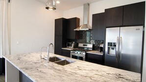 Una cocina moderna con encimera de mármol, electrodomésticos de acero inoxidable y armarios oscuros.