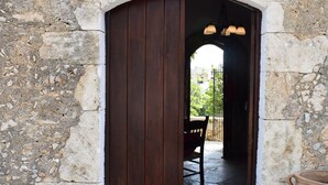 Un arc en pierre menant à une porte en bois, un balai et un grand pot en terre cuite.