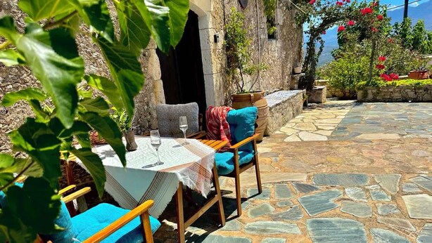Un espace extérieur aménagé avec un sol en pierre, une table avec deux verres et une chaise dotée d’un coussin bleu.