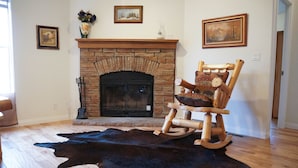Una habitación con chimenea de piedra, una mecedora de madera y un tapete de cuero negro.