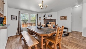 Un comedor con mesa de madera y bancos, una chimenea y vistas por un ventanal grande.