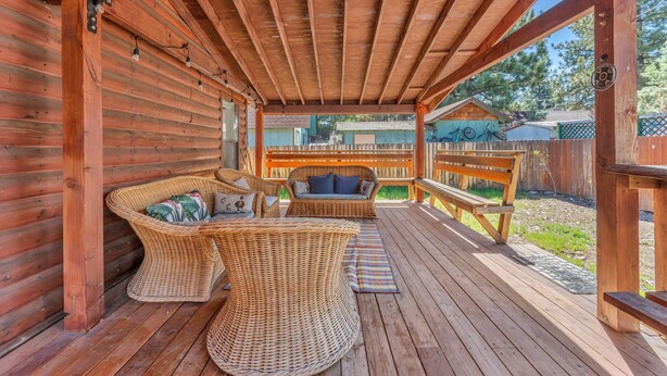 Una terraza de madera con mobiliario de mimbre y una banca.