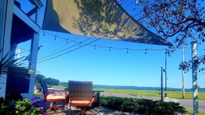 An outdoor seating area with two wicker chairs and a table, a large shade sail, and a view of the ocean. - City Amenities, Casco Bay Sunrises and Natural Beauty (Portland)