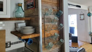 A kitchen with wooden shelves holding plates, a blue vase, and a wall-mounted glass rack. - City Amenities, Casco Bay Sunrises and Natural Beauty (Portland)
