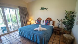 Quarto de hotel com uma cama grande, varanda com vista, peixe decorativo na parede e planta em vaso.