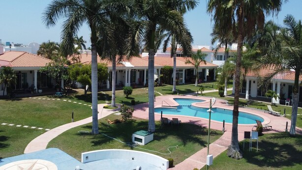 Área de piscina com palmeiras, uma fonte e um edifício com telhado de azulejos ao fundo.