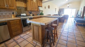 Uma cozinha com armários de madeira, uma ilha grande com banquetas e uma área de jantar com mesa e cadeiras.