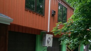 Ein Gebäude mit einer grünen Garagentür, einer großen Wandklimaanlage und einer Treppe, die zu einer Tür hinaufführt.