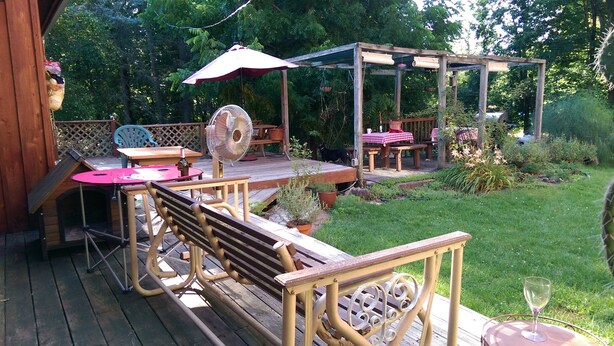 Ein möblierter Patio-Bereich im Freien mit Holzmöbeln, einem Ventilator und einer Pergola mit Tischen und Stühlen.