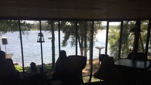 Una habitación tenuemente iluminada con vistas a un lago, que incluye una mesa y sillas orientadas hacia la ventana.
