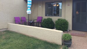 A building with a beige exterior, a black door, and a window. There are two purple chairs and a blue and white striped umbrella.