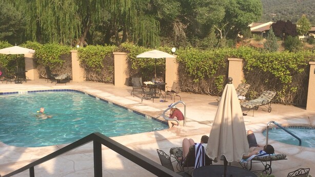 A swimming pool with lounge chairs and umbrellas, surrounded by greenery and hills.
