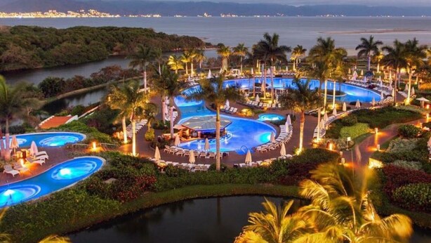 Un resort con varias piscinas, palmeras y vistas al océano.