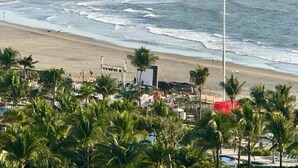 Una playa con arena, palmeras y algunos edificios al fondo.