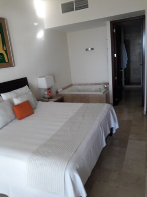 Une chambre d’hôtel avec un grand lit, une table de chevet, une lampe, une salle de bain avec une baignoire et une douche.
