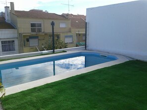 A swimming pool with a surrounding fence, adjacent to a building with a tiled roof. - Rio ... Beaches ... Lisbon, Ideal for families with children and pets. (Almada)