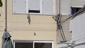 A patio area with a table and chairs, a green umbrella, and a building with white shutters and a garage door. - Rio ... Beaches ... Lisbon, Ideal for families with children and pets. (Almada)