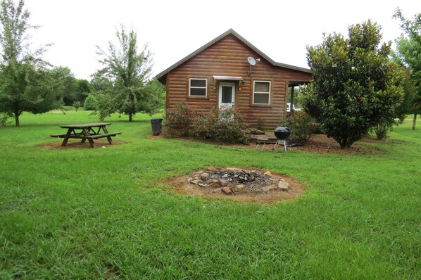 Una cabaña de madera con un pozo de fuego en el patio, rodeada de árboles y una mesa de picnic.