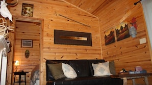 A cozy cabin interior with a wooden interior, a black leather sofa, a small table with a lamp, and a mounted deer skull. - Morningstar Cabin Caddo River. GREAT VALUE!!!!!!!!!!! River access!! (Glenwood)