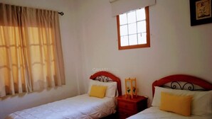 A bedroom with two beds, each with a red headboard, white bedding, and a yellow pillow. There is a window with a wooden frame and a curtain. - Apartment Clary in Gomera with Unique Views, Close to Beach (Vallehermoso)