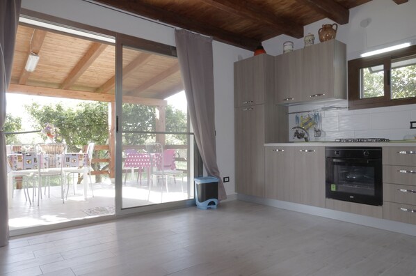 A modern kitchen with wooden cabinets, a built-in oven, and a sliding glass door leading to an outdoor patio. - Comfortable to the Sea, House (Contrada Fiori Sud)