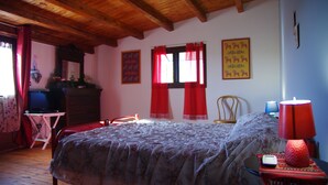 A bedroom with a wooden ceiling, a bed with a floral bedspread, a dresser, a chair, a desk with a computer, and two windows with red curtains. - Comfortable to the Sea, House (Contrada Fiori Sud)