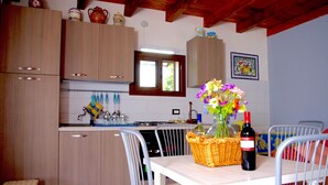 A kitchen with wooden cabinets, a dining table with chairs, a vase of flowers, and a bottle of wine. - Comfortable to the Sea, House (Contrada Fiori Sud)