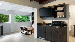 A modern kitchen with dark cabinetry, a flat-screen TV, and a dining area with a view of greenery.