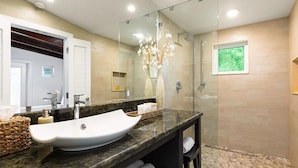 A modern bathroom with a large sink, a glass shower enclosure, and a small window with a view of greenery.