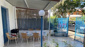 A covered outdoor dining area with a table and chairs, a blue gate, and a street view in the background. - Blue house 500m from the beach of Porto Cesareo (Porto Cesareo)