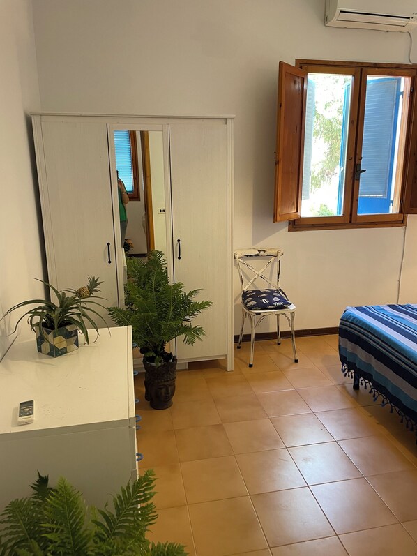 Una habitación pequeña y ordenada con una cama, una silla, un armario y dos plantas en macetas.