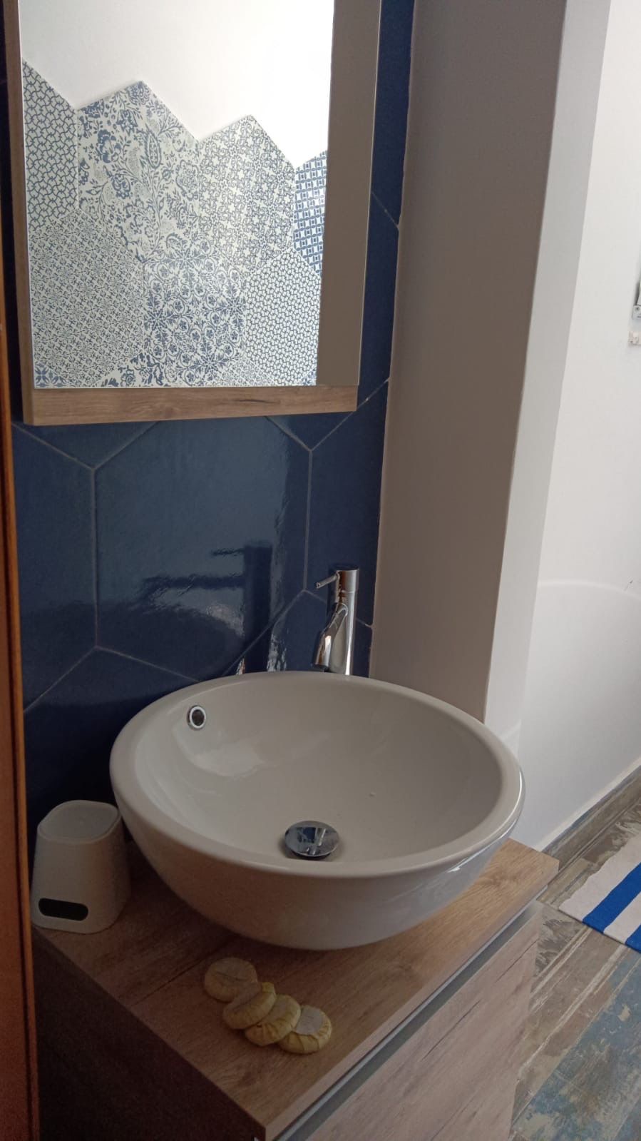 Ein Badezimmer mit einem weißen Waschbecken, dunkelblauen Fliesen und einer Holz-Kommode.