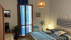 A bedroom with a bed, a desk, a chair, a potted plant, a fan, and a window with curtains. - Blue house 500m from the beach of Porto Cesareo (Porto Cesareo)