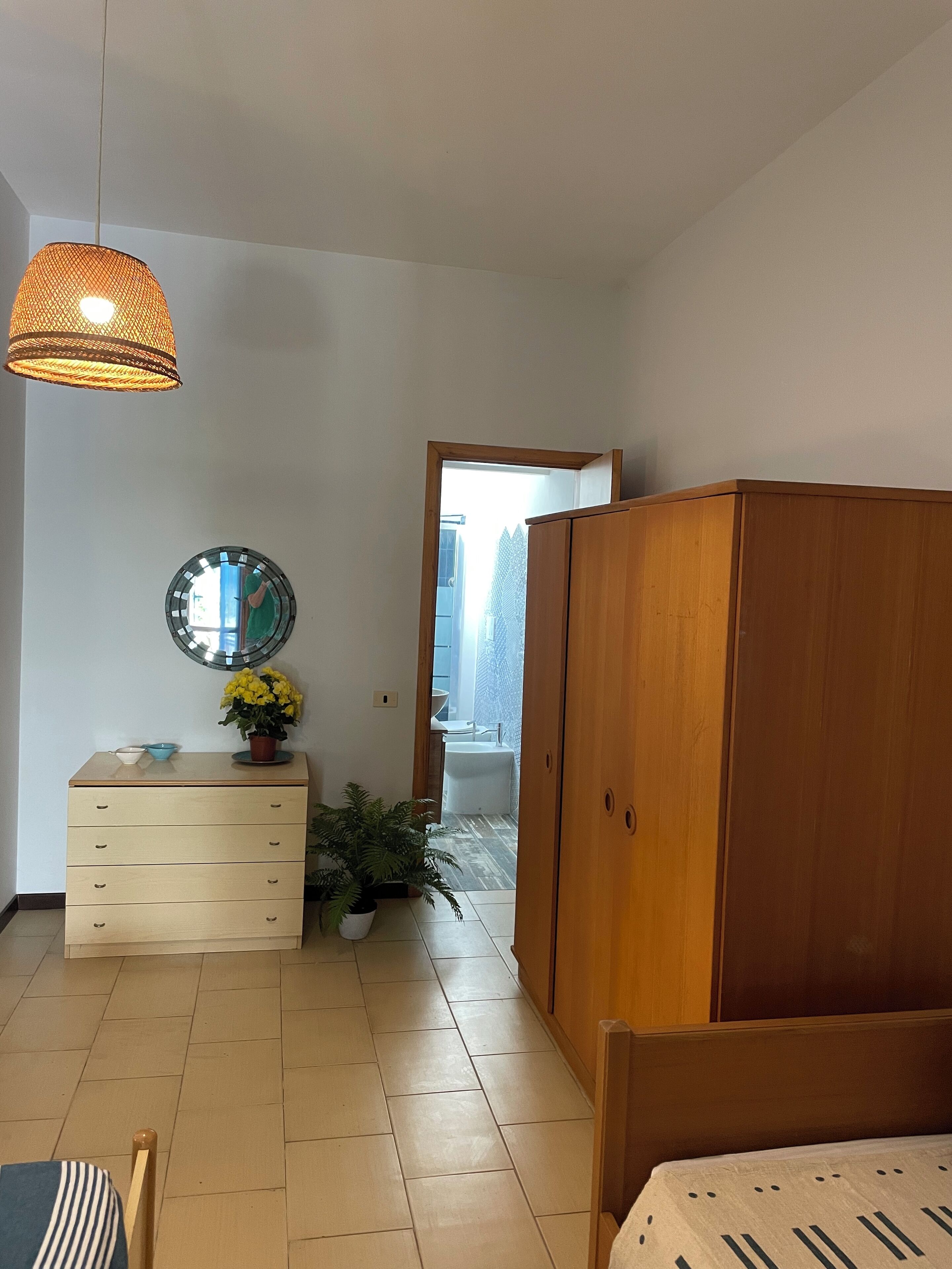 Un dormitorio con un armario de madera, una cama, un tocador y un espejo, además de una lámpara colgante.