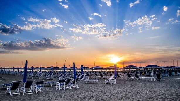 A beach with rows of sun loungers and umbrellas, a pier in the background, and the sun setting over the horizon. - Foscolo 1, 100m from the beach (Viareggio)