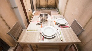 A dining table set with plates, cutlery, and a pot, surrounded by chairs in a small, enclosed space with a tiled floor and a wall with climbing plants. - Foscolo 1, 100m from the beach (Viareggio)