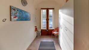 A hallway with a painting, a door with windows, a chair, and a trash bin. - Foscolo 1, 100m from the beach (Viareggio)