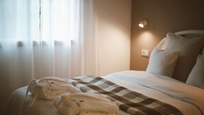 Una cama bien tendida con una colcha a cuadros, un par de batas de baño blancas y una lámpara de noche.