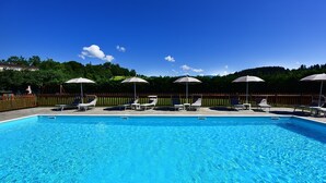 A rectangular swimming pool with clear blue water, surrounded by white lounge chairs and umbrellas. - AGRITURISMO LA PIETRAIA (Poppi)