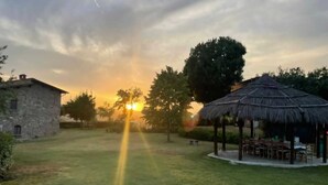 A stone building, a thatched pavilion, and a grassy area with a sunset in the background. - AGRITURISMO LA PIETRAIA (Poppi)