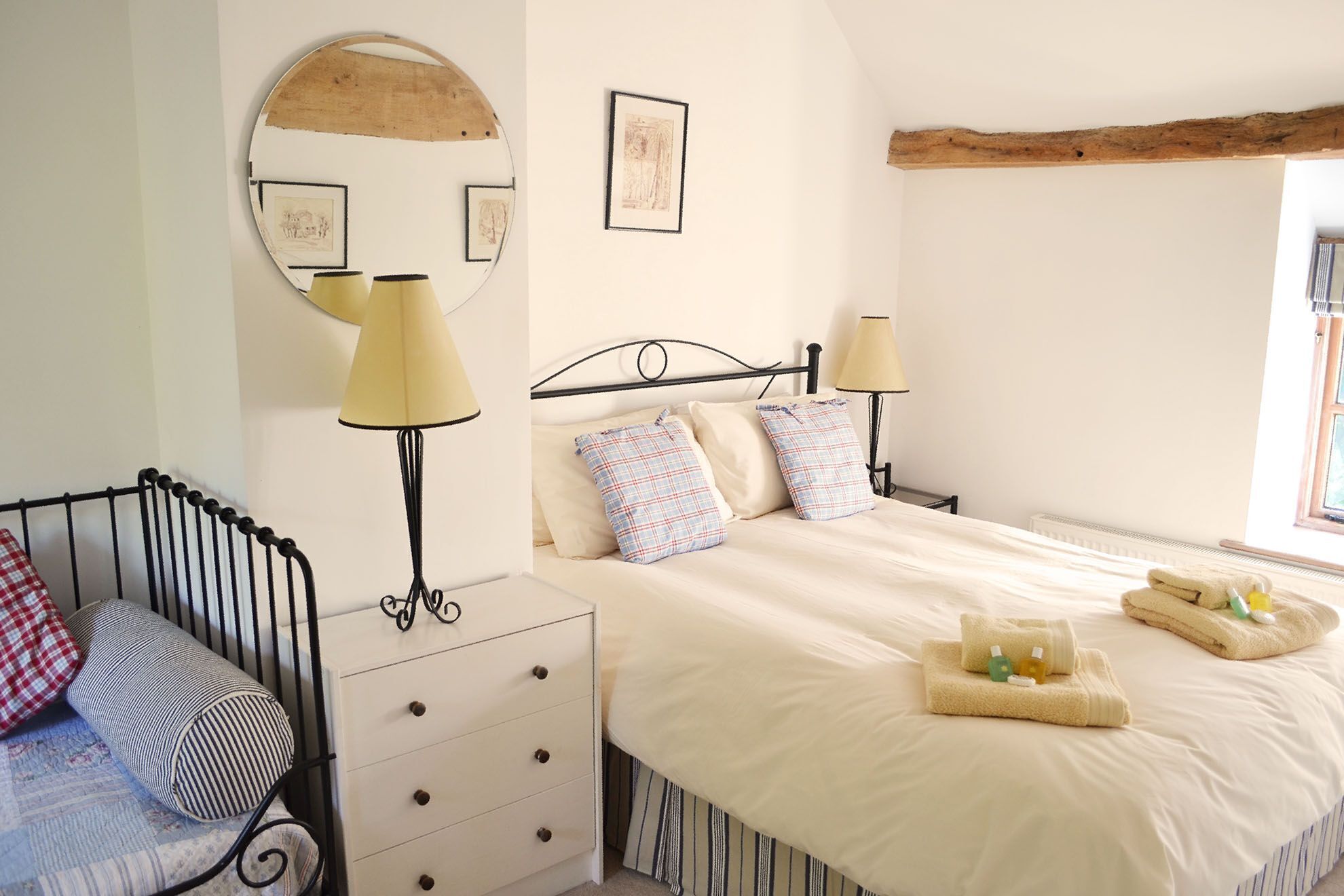 A bedroom with a bed, two bedside lamps, a dresser, a mirror, and a window.