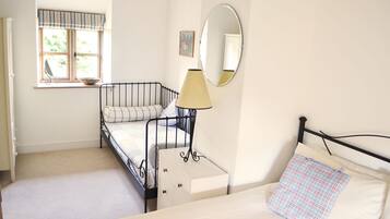 A room with two beds, a window with a view of greenery, a mirror, and a lamp.
