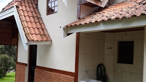 Una casa con techo de tejas, sección inferior de ladrillo y un pequeño baño contiguo con lavamanos y manguera.
