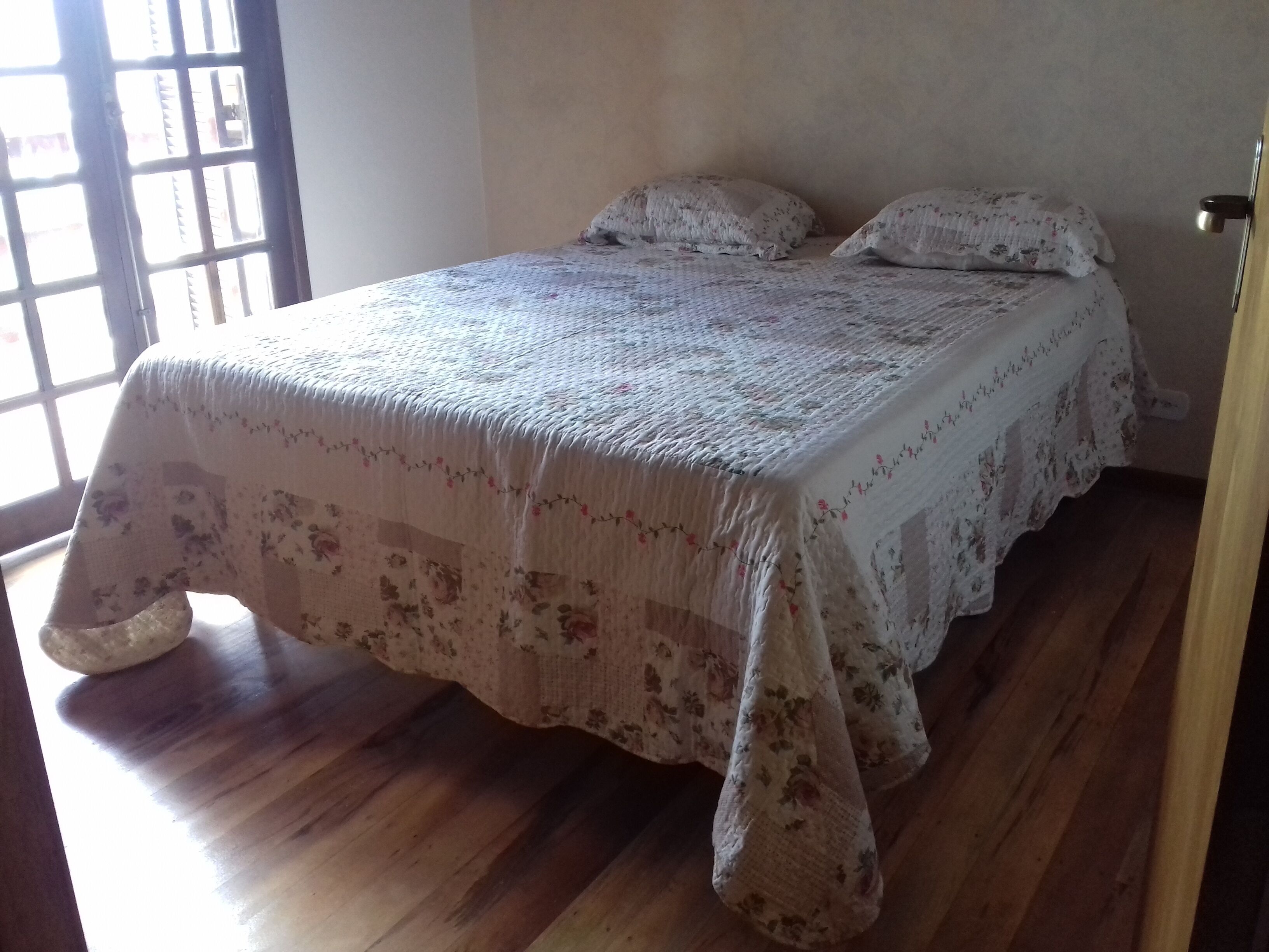 Une chambre à coucher avec un lit recouvert d’une couvre-lit à motifs floraux, un plancher en bois et une fenêtre à carreaux.