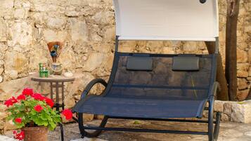 A reclining chair with a white canopy, a small table with a vase of flowers, and a potted plant with red flowers.