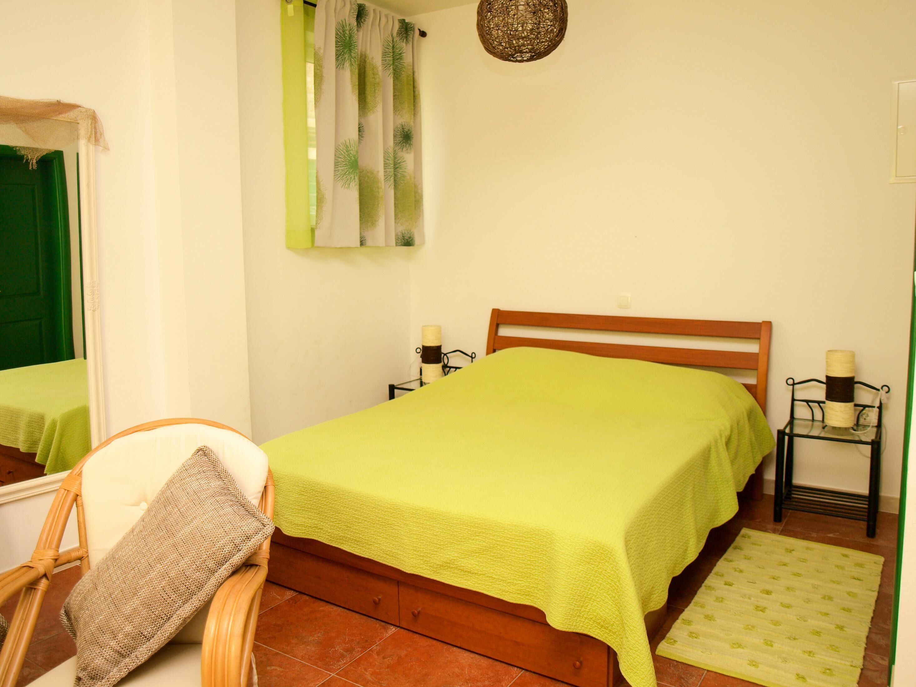 Une petite chambre à coucher, bien rangée, avec un lit simple, une chaise, une table de chevet et un petit tapis.