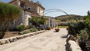 Un edificio de piedra con un patio techado, plantas en macetas y un sendero de piedra que conduce a la entrada.